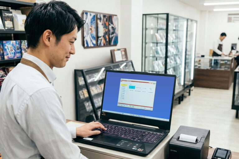 トレカショップのレジカウンターで、店員がMOOV POSシステムを操作している様子。背景には棚に並んだトレカや看板が見える。
